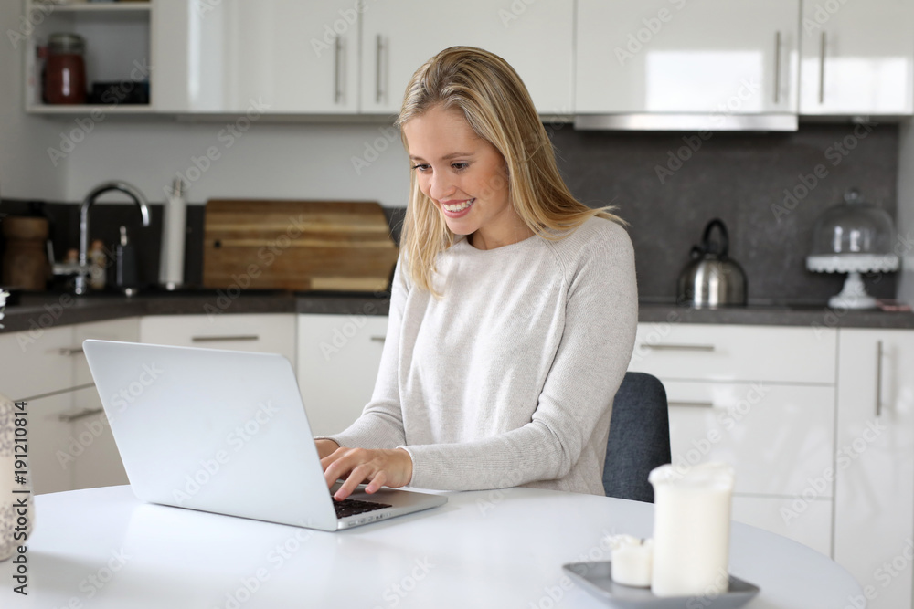 Hübsche blonde Frau sitzt an an einem Laptop und lacht