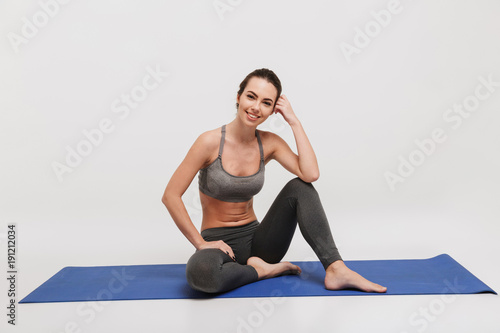 young woman sitting relaxed on yoga mat isolated on white