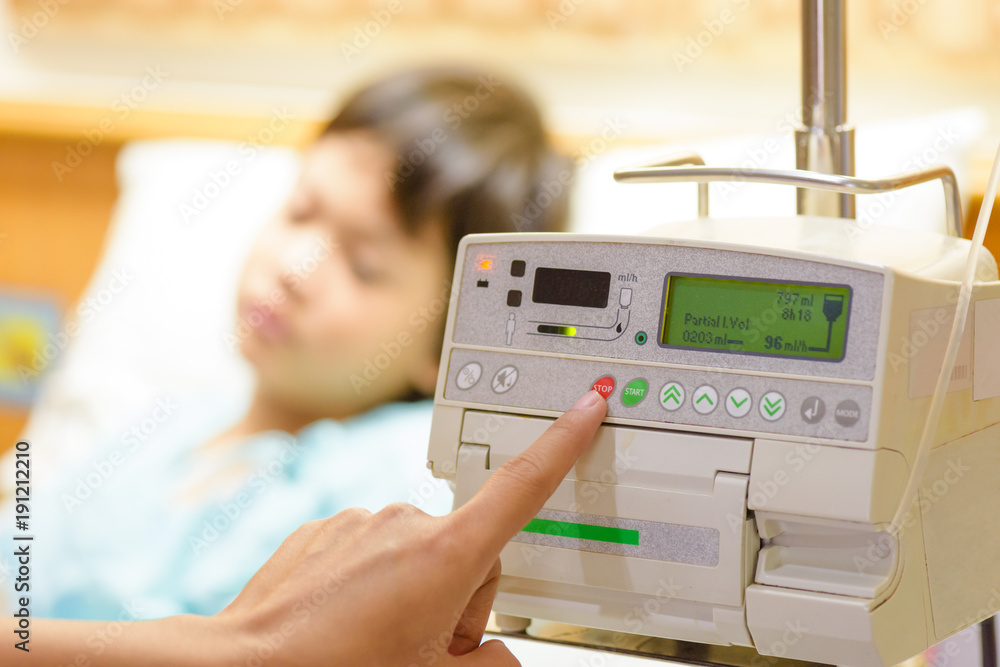 Nurse's hand pressing on infusion pump intravenous IV drip on kid admitted background. Health care concept. Nurse's hand pressing on infusion pump intravenous IV drip on kid admitted background. Health care concept.