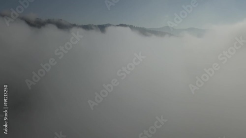 Flying over fog and clouds in Carpathians mountains near by Dzembronya village at sunny day, Ukraine