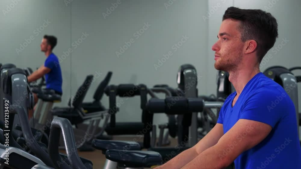 A young fit man trains on an exercise bike in a gym - closeup from the side A young fit man trains on an exercise bike in a gym - closeup from the side