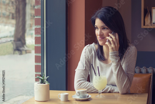 Beautiful young woman drink coffee and talk on the smartphone at cafe