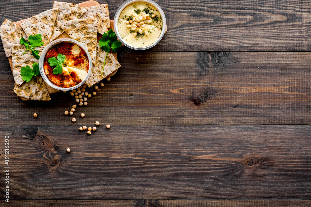 Serve hummus. Bowl with dish near pieces of crispbread on dark wooden background top view copy space