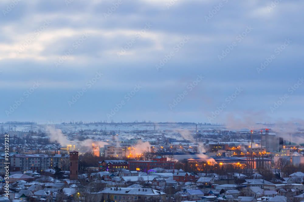 Frosty winter morning vapor comes from the pipes of the plant over the city covered with snow.