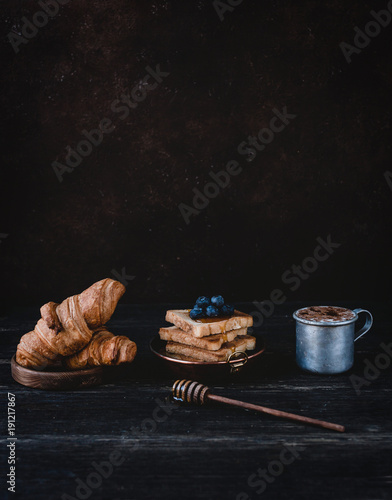 close up view of croissants, toasts with blueberries and drink on wooden tabletop