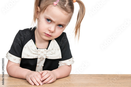 Portrait of a serious baby girl sitting at a table close-up, isolated on a white background photo