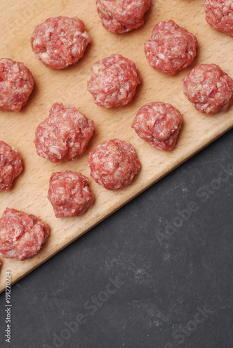 Raw Balls from Raw Beef Meat on Wooden Board over Dark Background. Copy space. Food Recipe, vertical Image.