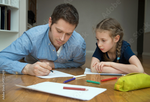 Father and her daughter drawing on the floor.