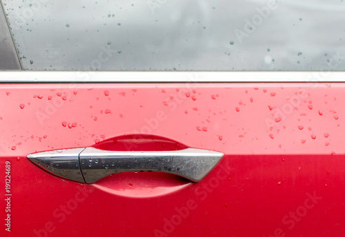 Water droplets on the handle of a red car.