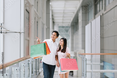 Happy Asian couple holding colorful shopping bags and enjoying shopping, having fun together in mall. Consumerism, love, dating, lifestyle concept