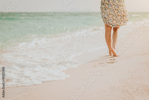 woman walking on beach leaving footprints in the sand during sunset