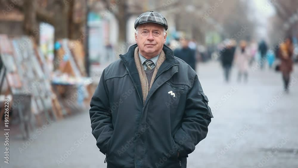 A wonderful view of an old man dressed in a black zipup coat and a woollen flat cap. He goes along a park alley with pictures in autumn. A wonderful view of an old man dressed in a black zipup coat and a woollen flat cap. He goes along a park alley with pictures in autumn.