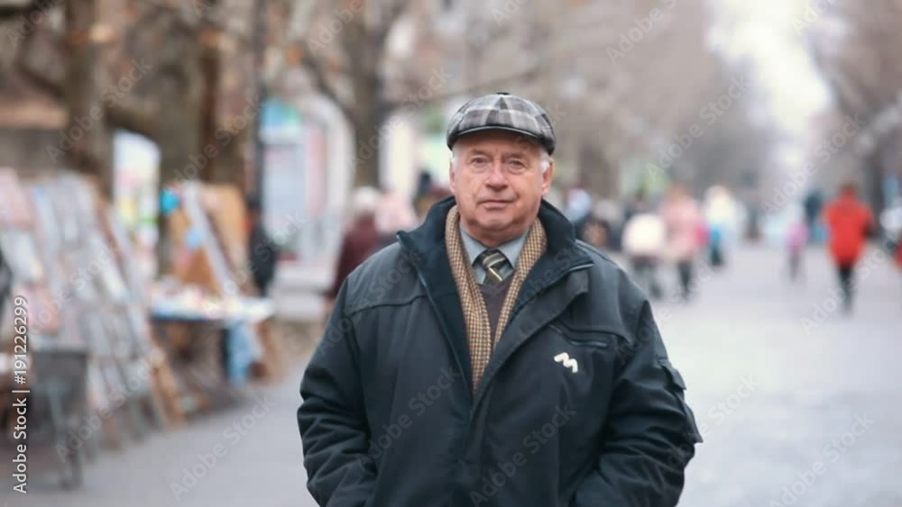 An inspiring view of an old man dressed in a black zipup coat and a woollen flat cap. He walks along a park alley with pictures in autumn. An inspiring view of an old man dressed in a black zipup coat and a woollen flat cap. He walks along a park alley with pictures in autumn.