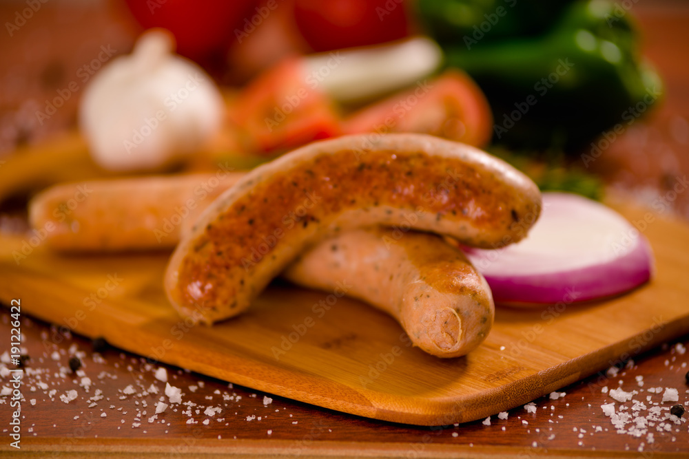 Close up of delicious grilled sausages and vegetables, tomato, onio, green pepper and rosemary spices on a wooden background in rustic style Close up of delicious grilled sausages and vegetables, tomato, onio, green pepper and rosemary spices on a wooden background in rustic style