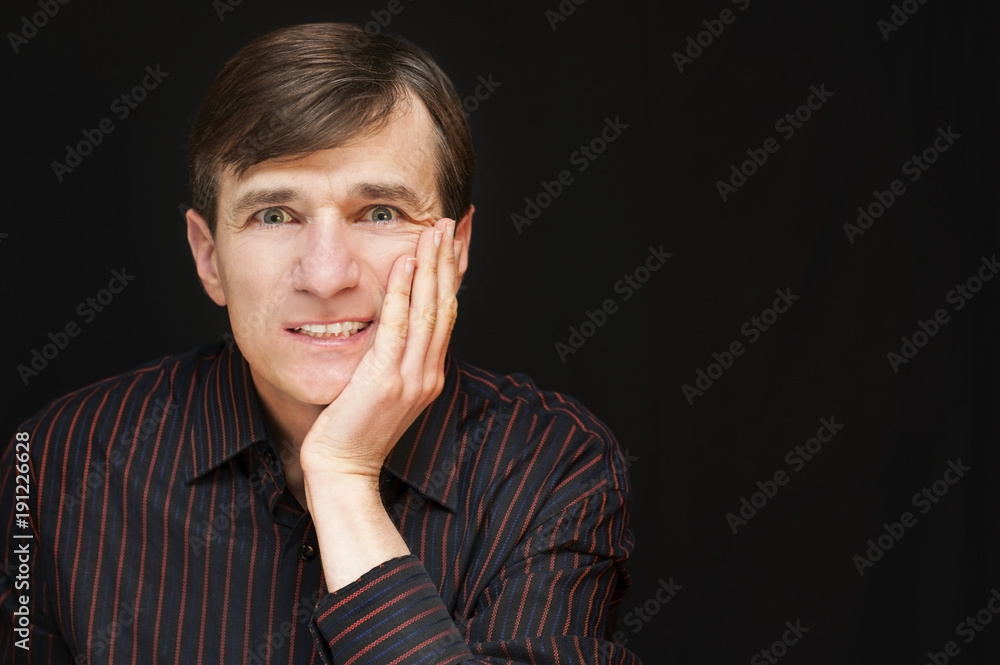 A middle-aged man with a sad, angry face holds his hand on his cheek because he has a toothache A middle-aged man with a sad, angry face holds his hand on his cheek because he has a toothache