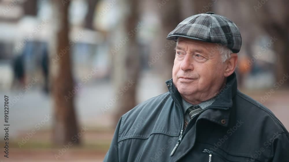 A wonderful view of a senior man dressed in a black zipup coat and a woollen flat cap. He stands on a nice park alley and waits in autumn. A wonderful view of a senior man dressed in a black zipup coat and a woollen flat cap. He stands on a nice park alley and waits in autumn.