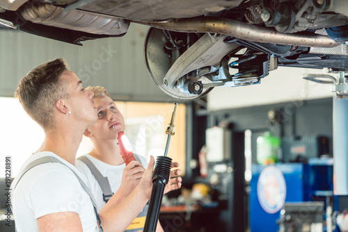 Side view of a skilled auto mechanic, replacing the shock absorbers of a lifted car while working together with his colleague in a modern automobile repair shop