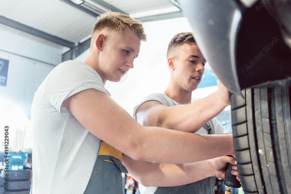 Low-angle view of a skilled auto mechanic working together with his colleague at the tuning of a car in a modern automobile repair shop, with reliable employees Low-angle view of a skilled auto mechanic working together with his colleague at the tuning of a car in a modern automobile repair shop, with reliable employees