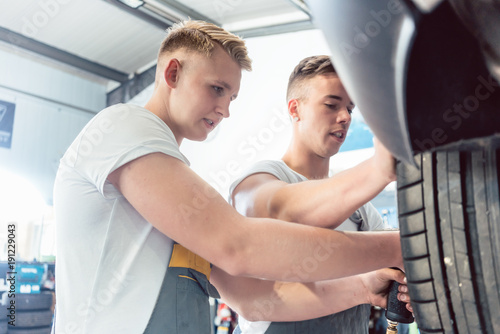 Low-angle view of a skilled auto mechanic working together with his colleague at the tuning of a car in a modern automobile repair shop, with reliable employees