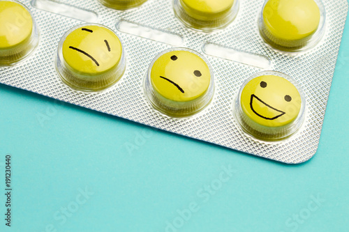 Yellow pills and funny faces in a blister on a blue background. The concept of antidepressants and healing