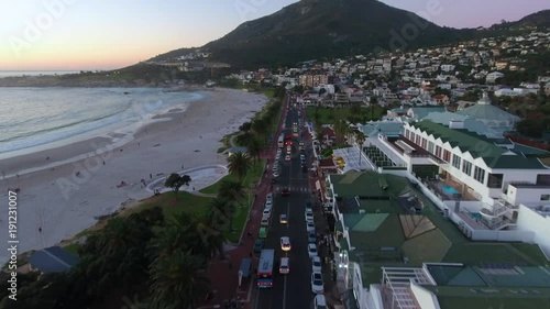 Aerial view above Camps Bay in Cape Town South Africa at sunset with the ocean, cars and businesses below.