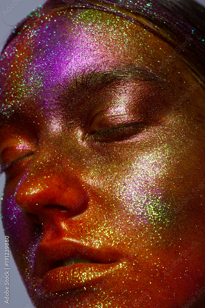 Close up of a portrait of the girl with an unusual make-up showing space. Gloss and shine, stars and constellations on a face. Body art, studio of beauty and art