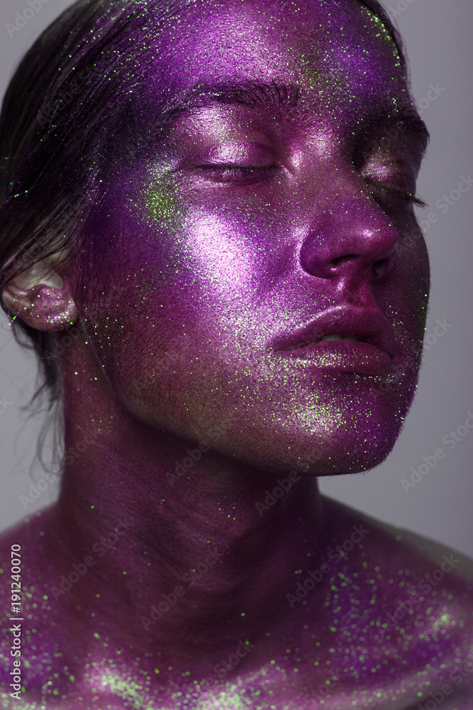 Portrait of beautiful woman with sparkles on her face. Girl with art make up in color light. Fashion model with colorful make-up