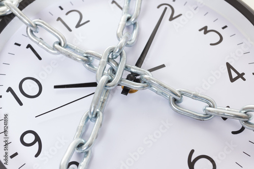 Chain holding an alarm wall clock, time management concept