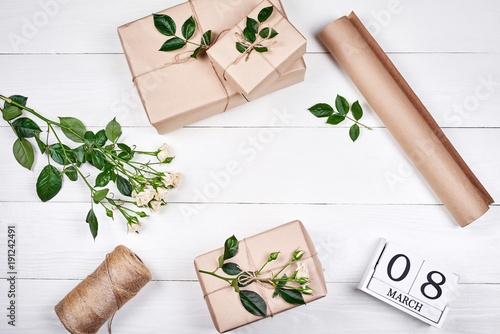 Gift wrapping background, copy space. Rolls of kraft wrapping paper, twine, branch of roses, gift boxes on wooden background, free space. Flat lay, top view. Womens Day, March 8, Easter, spring