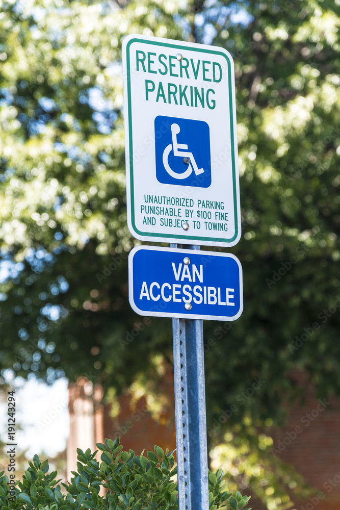 Vertical shot of a handicapped parking sign with a 15 mile per hour sign below it.  Out of focus trees and a building in the background.