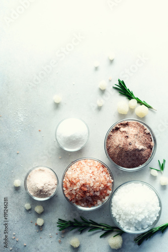 Mix of different salt types on grey concrete background. Sea salts, black and pink Himalayan salt crystals, powder, rosemary. Salt crystal balls from Dead sea. Copy space. Top view. photo