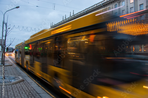 The motion of a blurred bus on the avenue at dusk.