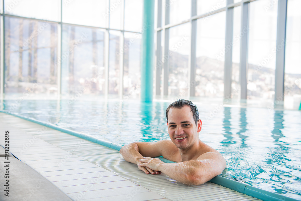 Young man relaxing on a luxury rooftop swimming pool and smiling at camera at five star hotel spa