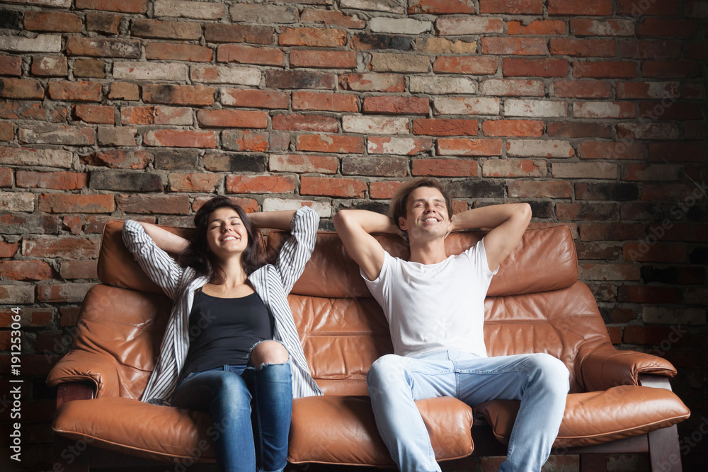 Young happy couple relaxing on comfortable leather couch at home, relaxed smiling man and woman resting on sofa in loft interior breathing fresh air meditating together, no stress, positive thinking Young happy couple relaxing on comfortable leather couch at home, relaxed smiling man and woman resting on sofa in loft interior breathing fresh air meditating together, no stress, positive thinking