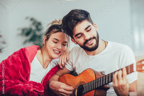 Young couple are playing guitar and happy smiling while sitting on couch at home