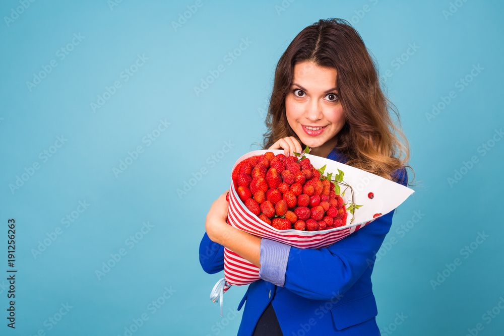 Young woman holding bouquet of strawberries on blue background. Young woman holding bouquet of strawberries on blue background.