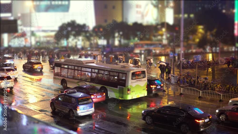 Cars and buses drive down the street with illuminated advertising and flashlights, people with umbrellas are walking along the road Cars and buses drive down the street with illuminated advertising and flashlights, people with umbrellas are walking along the road