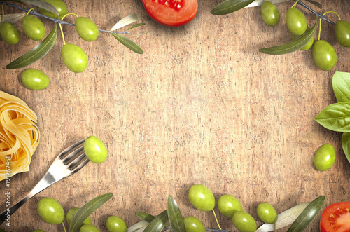 fork with olive and tomatoes and pasta on wooden table