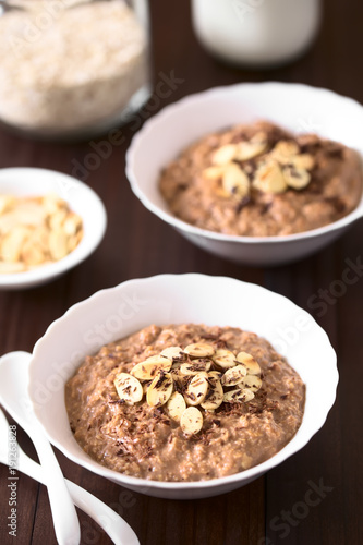 Chocolate oatmeal or oat porridge with toasted almond slices and grated chocolate on top served in small bowls, photographed with natural light (Selective Focus, Focus in the middle of the first bowl)