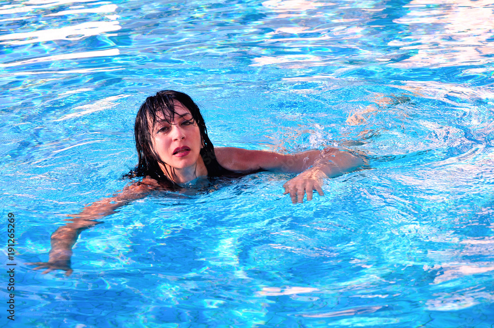 A beautiful girl is swimming in the swimming pool with blue awter.