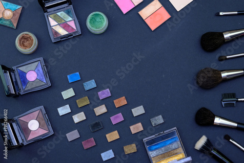 Set of make-up brushes and decorative cosmetics on dark blue colored composed background. Top view point, flat lay, space for text.