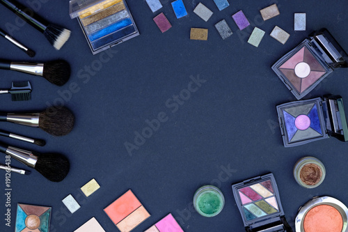 Set of make-up brushes and decorative cosmetics on dark blue colored composed background. Top view point, flat lay, space for text.