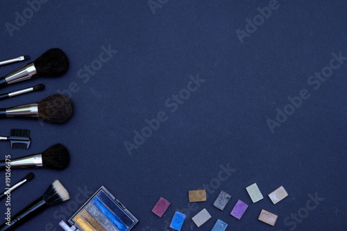 Set of make-up brushes and decorative cosmetics on dark blue colored composed background. Top view point, flat lay, space for text.