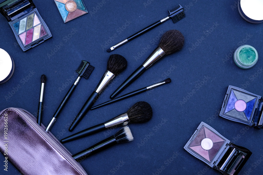 Set of makeup brushes and decoradive cosmetics with purple bag on dark blue colored composed background. Top view point, flat lay Set of makeup brushes and decoradive cosmetics with purple bag on dark blue colored composed background. Top view point, flat lay