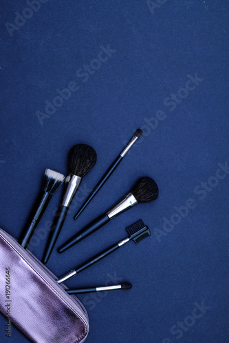 Set of makeup brushes with cosmetics bag on dark blue colored composed background. Top view point, flat lay