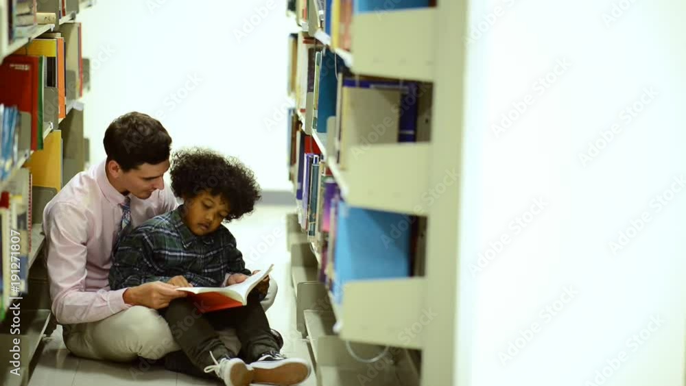 Small children study with teacher. Young African american reading book in library with white male teacher. Education concept. Small children study with teacher. Young African american reading book in library with white male teacher. Education concept.