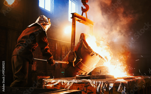 Workers operates at the metallurgical plant. The liquid metal is poured into molds. Worker controlling metal melting in furnaces. photo