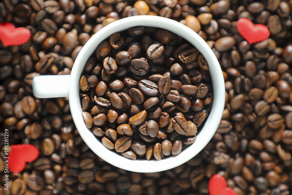 White cup with coffee beans on the coffee beans background.