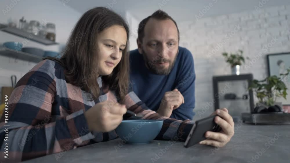 Father and daughter talking, eating and watching movie on smartphone
Father and daughter talking, eating and watching movie on smartphone