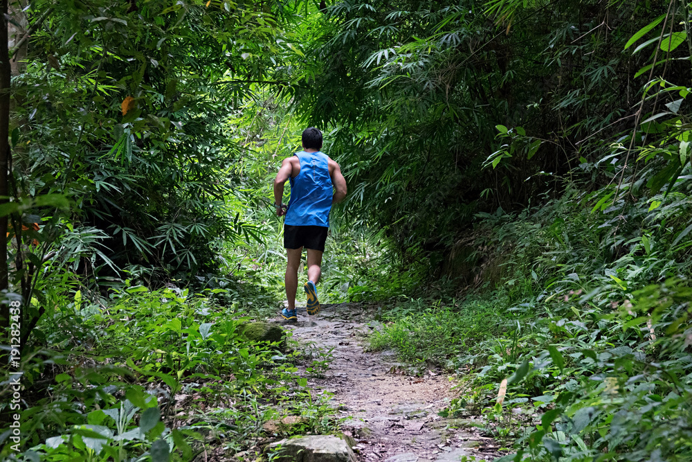 Athletic runner running on tropical forest trail, dramatic tone